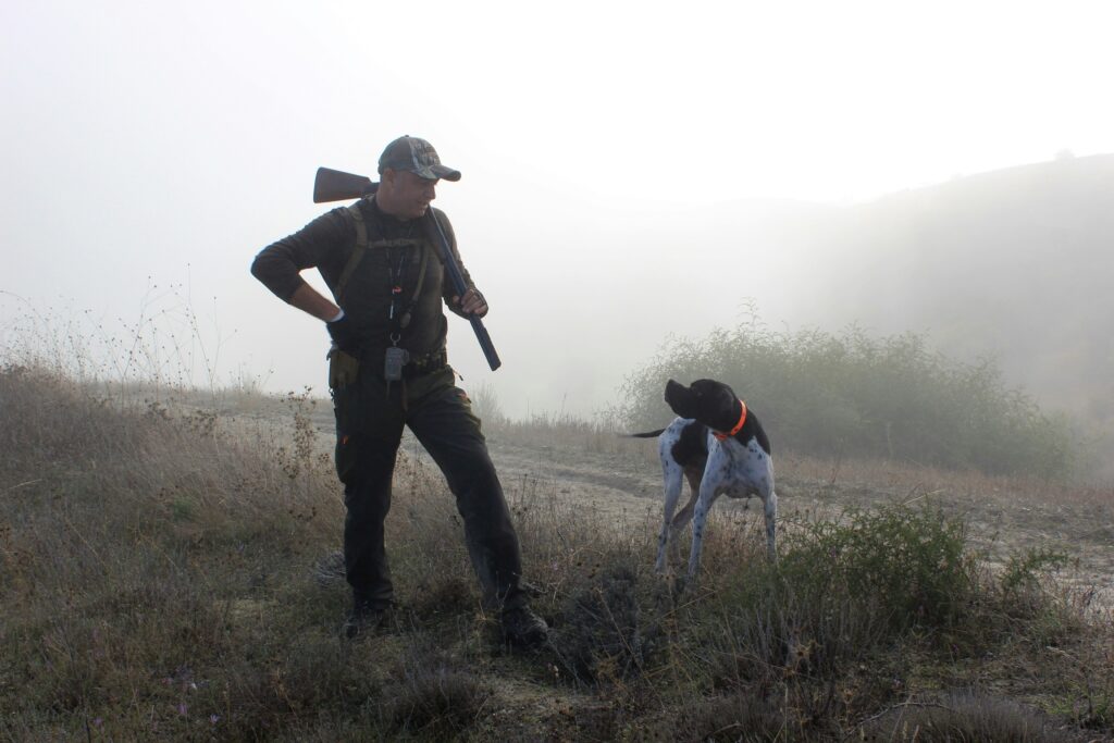 Jäger mit Vorstehhund im Morgennebel im Feld